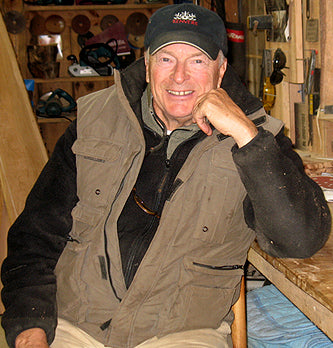 Photo of Ken Vermeulen, founder of Kenver sitting, smiling at Camera with left elbow posed on a work table and fist on his chin. 