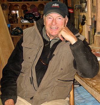 Photo of Ken Vermeulen, founder of Kenver sitting, smiling at Camera with left elbow posed on a work table and fist on his chin.