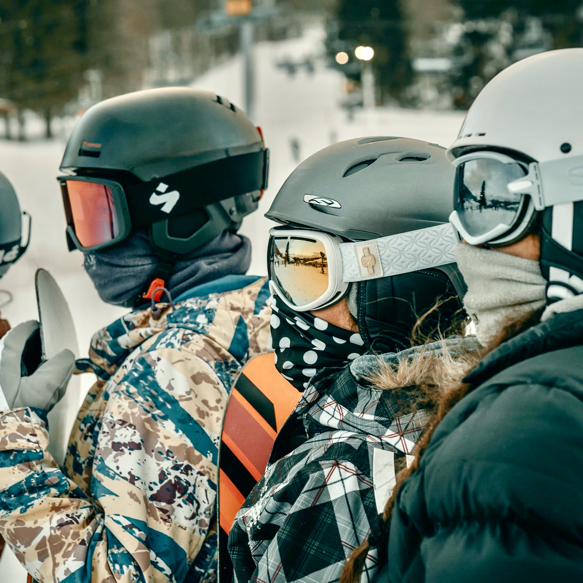Three people, men and women are standing in a row, with winter masks, helmets on, and goggles covering their face.