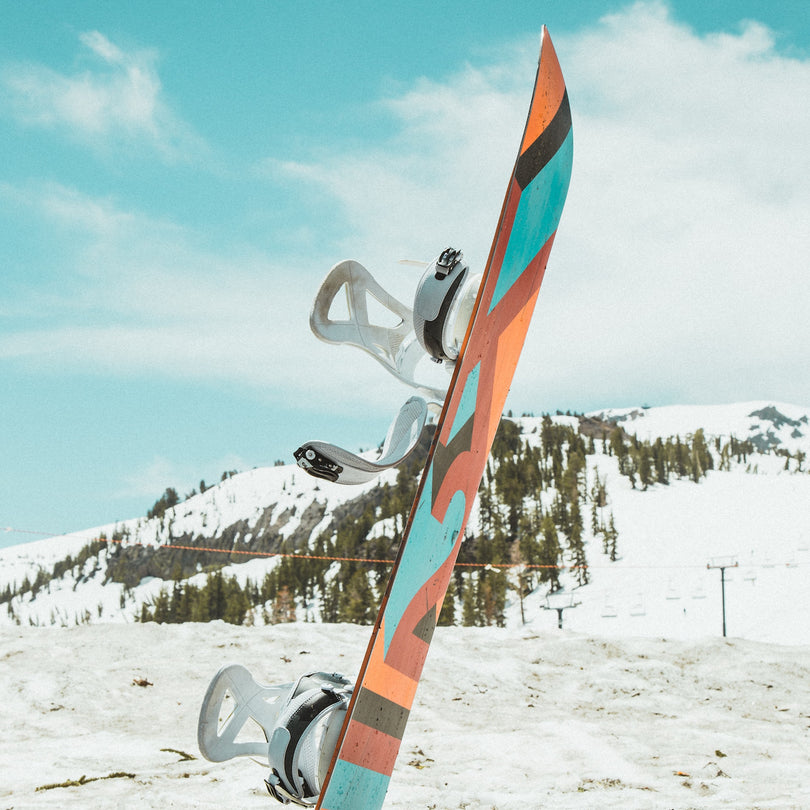 A snowboard sticking straight up out of the snow, with a snowy mountain in the background