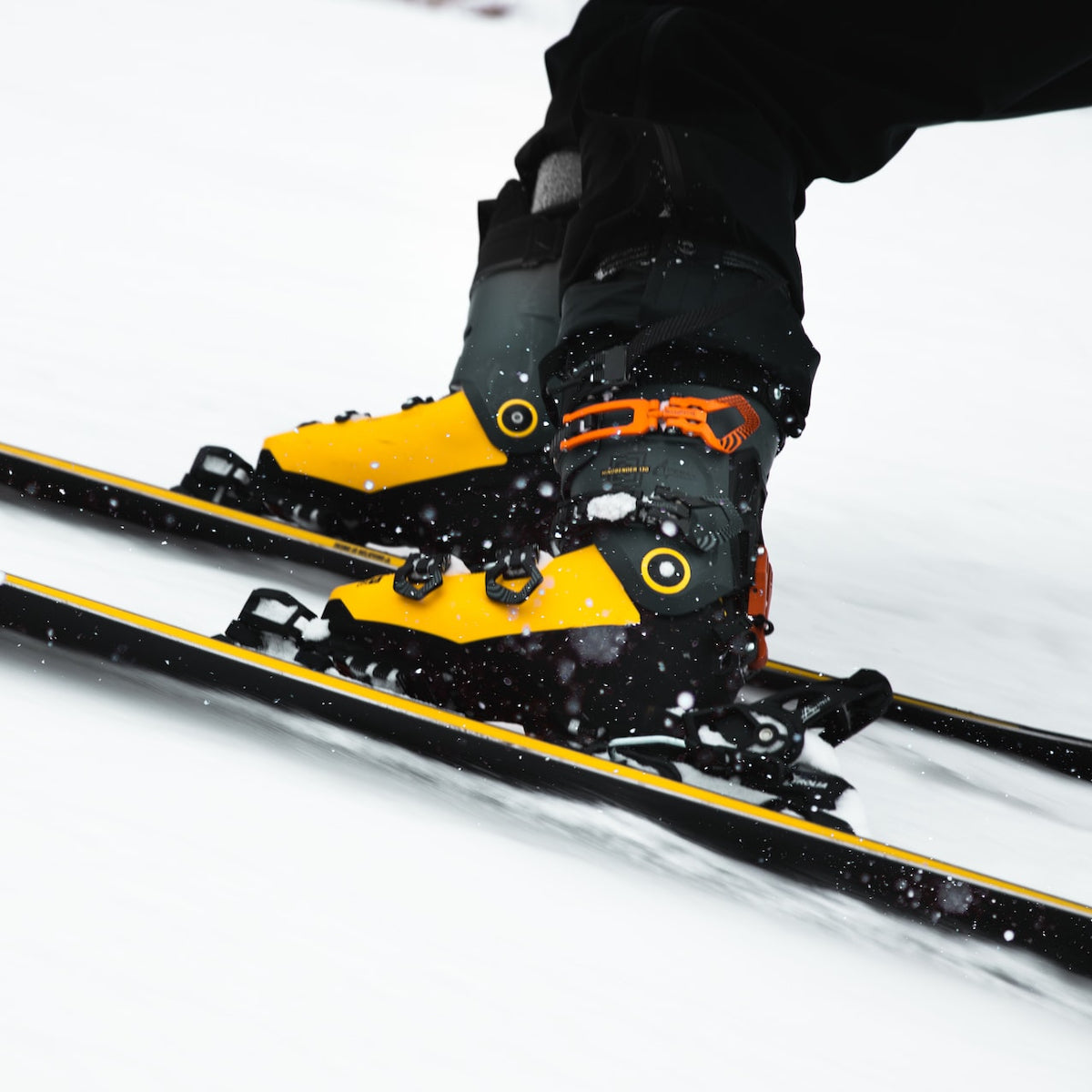 closeup photo of a person knee-down as they slow to a stop, focusing on the yellow pair of boots and skis.