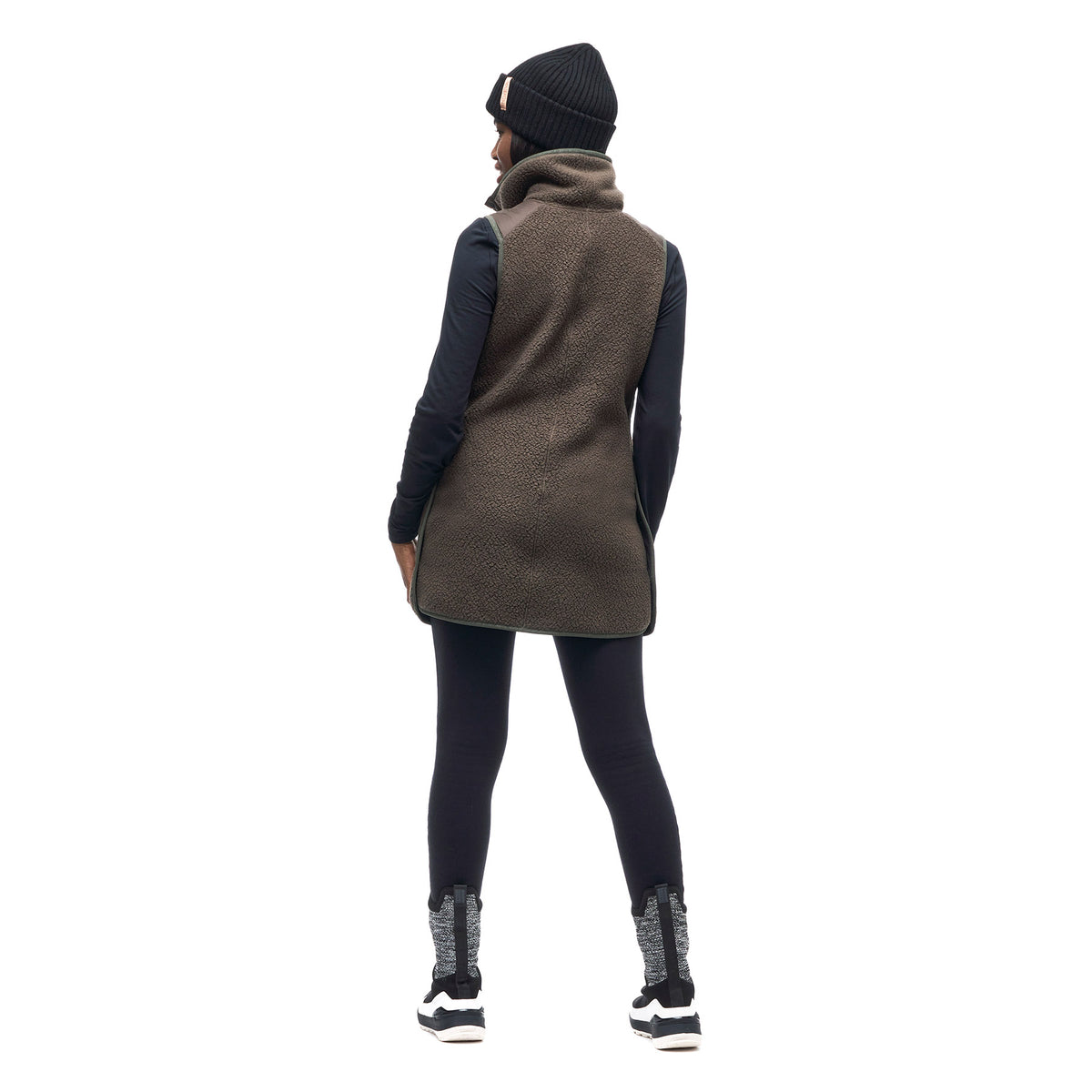 Image features a back facing photo of a model wearing the Indyeva Pecora Tunic in mocha with black leggings and a black beanie.