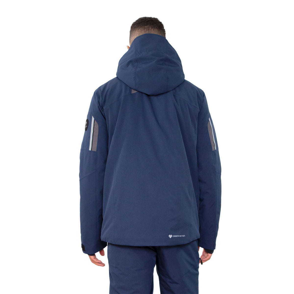 Image features the back of a male model wearing the Obermeyer Primo Jacket in admiral blue with navy blue ski pants.